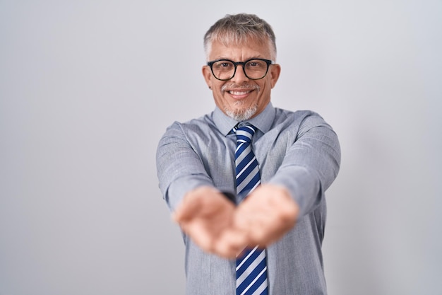 Spanischer Geschäftsmann mit grauen Haaren, Brille trägt, lächelt mit den Händen, den Handflächen zusammen, empfängt oder gibt Geste, hält und schützt