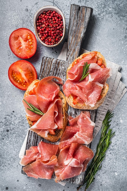 Spanischer Tapas-Toast mit Tomaten und gepökelten Scheiben Jamon Iberico-Schinken auf Holzbrett Grauer Hintergrund Ansicht von oben