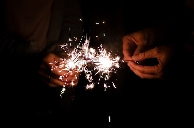 Foto sparkler luz llama ardiendo en manos de mujer amiga sosteniendo en el fondo de la noche