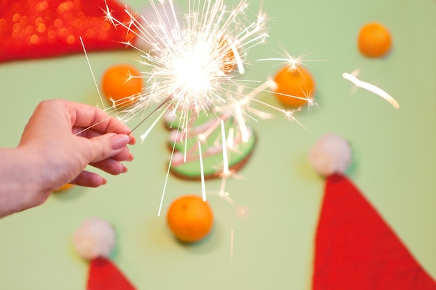 Sparkler na mão da mulher perto da luz de bengala do natal dos mandarines para comemorar no fundo verde