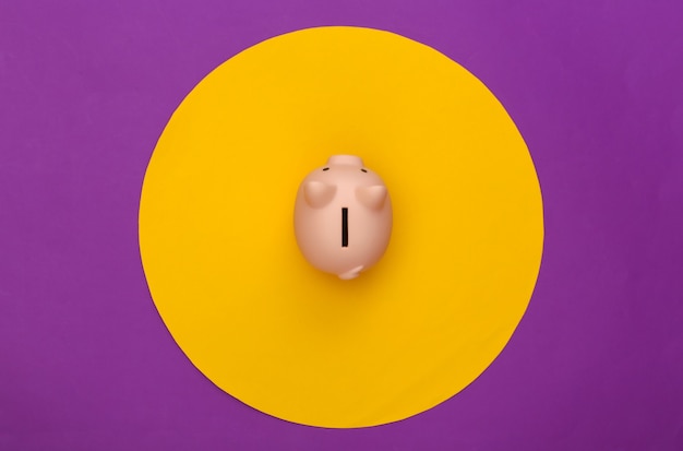 Sparschwein auf lila Hintergrund mit gelbem Kreis. Konzeptionelle Studioaufnahme. Minimalismus. Ansicht von oben