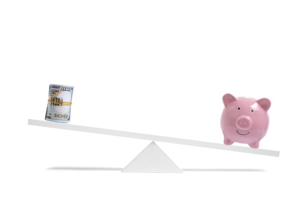 Sparschwein auf Waage überwiegt Rolle von Hundert-Dollar-Scheinen, auf weißem Hintergrund, Geschäft und Einsparungen.