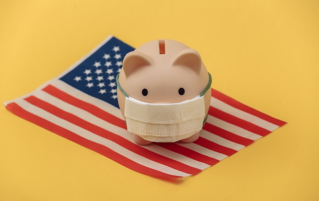 Sparschwein in medizinischer Maske mit der USA-Flagge auf gelbem Hintergrund. Covid-19-Pandemie