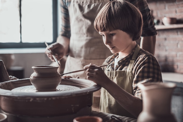 Spaß am Töpferkurs. Kleiner Junge, der im Töpferkurs auf Keramiktopf zeichnet