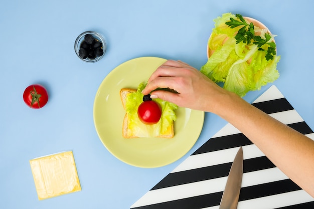 Spaß Essen Kunst für Kinder. Marienkäfersandwich an der blauen Wand. Wie man ein kreatives Frühstück für Kinder zu Hause macht. Schritt für Schritt Anleitung, Ansicht von oben.