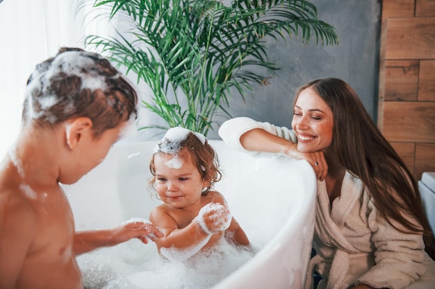 Foto spaß haben junge mutter hilft ihrem sohn und ihrer tochter zwei kinder beim waschen im bad