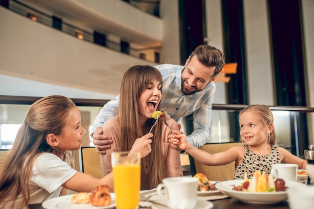 Spaß haben. Lächelnde Familie, die am Tisch sitzt und Spaß hat