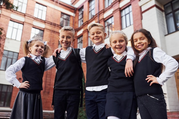 Spaß haben und sich gegenseitig umarmen. Gruppe von Kindern in Schuluniform, die sich im Freien in der Nähe des Bildungsgebäudes befindet.