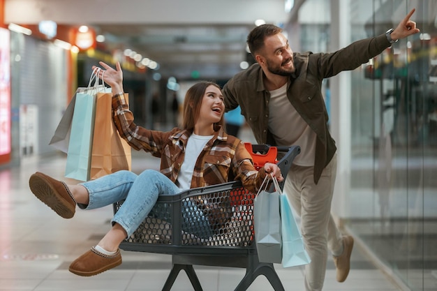 Spaß im Einkaufszentrum mit dem Einkaufswagen Ein junges Paar ist zusammen im Supermarkt