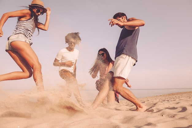 Spaß in Aktion. Gruppe fröhlicher junger Leute, die mit Fußball am Strand spielen