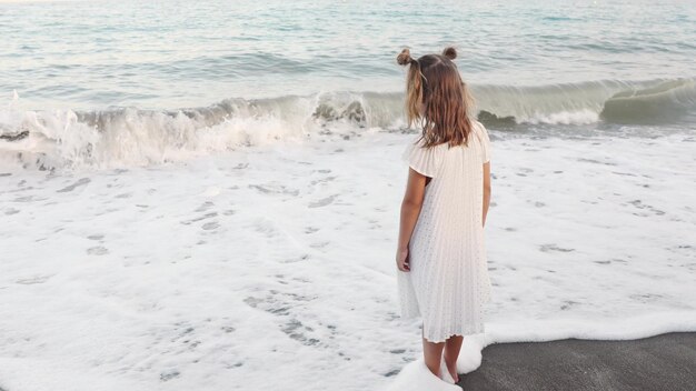 Foto spaß lächelndes kleinkind mädchen barfuß an der küste sand verbringen zeit am meer spielen meereswellen.