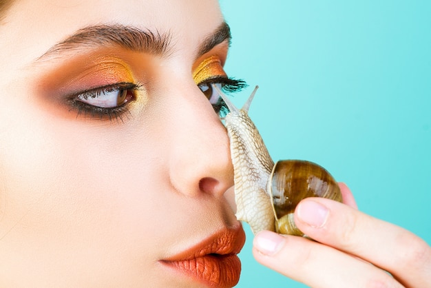 Spaß mit entzückender Schnecke. Kosmetik und Schneckenschleim. Modisches Make-up-Gesicht des Mädchens und niedliche Schnecke.