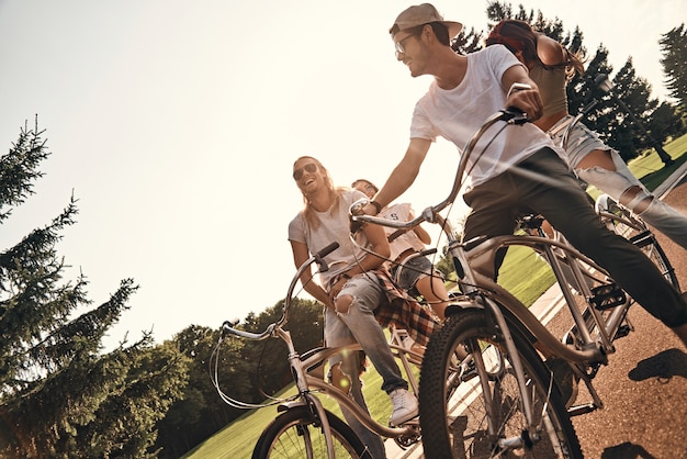 Foto spaß mit fahrrädern. gruppe glücklicher junger leute in freizeitkleidung, die beim gemeinsamen radfahren im freien lächeln