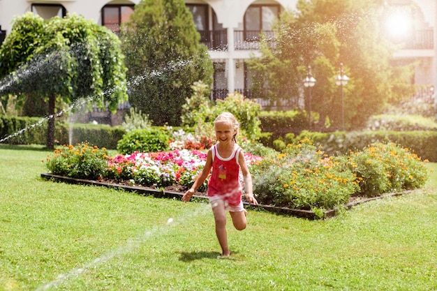 Spaß mit Gartensprinklern im Garten Kind läuft barfuß auf Gras Frohe Sommerferien