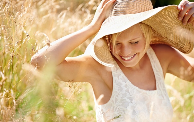 Spaß unter der Sonne Aufnahme einer schönen jungen Frau in einem Sonnenhut, die durch hohes Gras geht