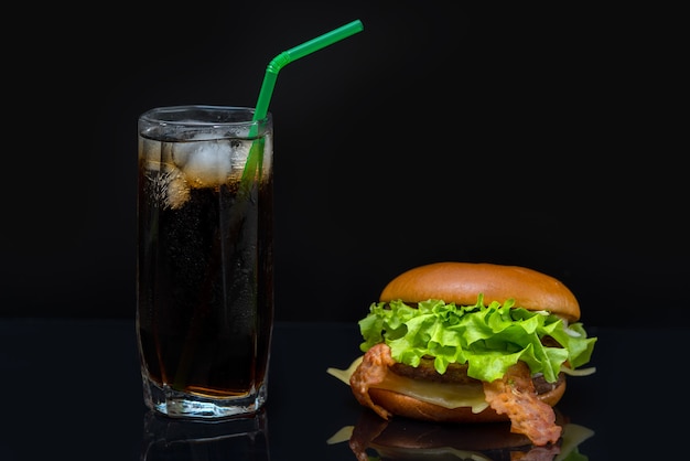 Speckburger gefüllt mit Salatblättern und hohem Glas Soda, das Eis enthält, das auf reflektierendem Tisch sitzt