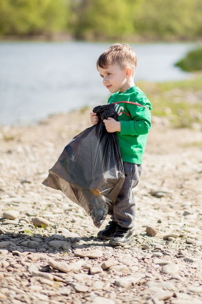 Speichern Sie Umweltkonzept, ein kleiner Junge, der Müll und Plastikflaschen am Strand sammelt, um in den Müll geworfen zu werden.