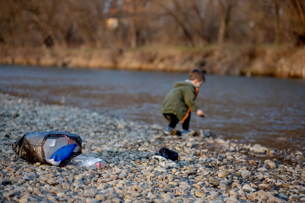Speichern Sie Umweltkonzept, ein kleiner Junge, der Müll und Plastikflaschen am Strand sammelt, um in den Müll geworfen zu werden