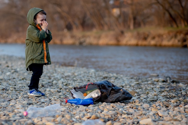 Speichern Sie Umweltkonzept, ein kleiner Junge, der Müll und Plastikflaschen auf dem Fluss sammelt, um in den Müll geworfen zu werden