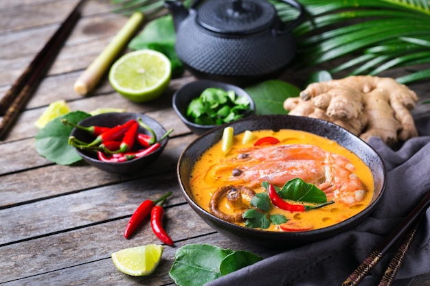 Speisen und Getränke, traditionelle thailändische Küche. Würzige tom yam kung, tom yum sour suppe mit garnelen, garnelen, kokosmilch, zitronengras und chilipfeffer in einer schüssel auf einem holztisch