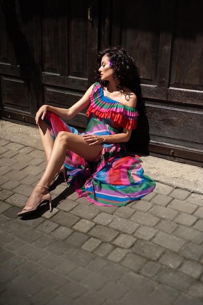 Spektakuläre sinnliche schöne europäische Frau mit gekräuselten dunklen Haaren in einem Sommerkleid in der Stadt