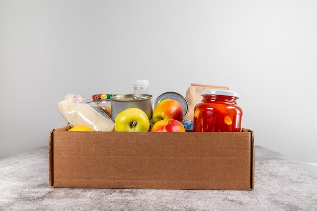 Spendenbox mit gesundem Naturkost, Obst, Müsli und Konserven auf einem grauen Tisch