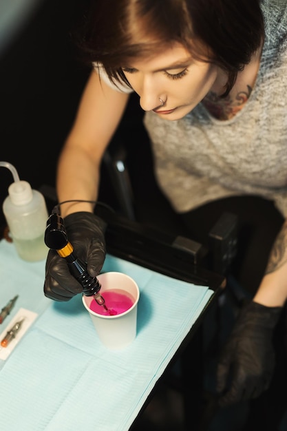 Spezialfarbe zum Tätowieren. Vorbereitung des professionellen Tätowierers zur Arbeit, Tinte mit Spezialmaschine nehmend, Nahaufnahme