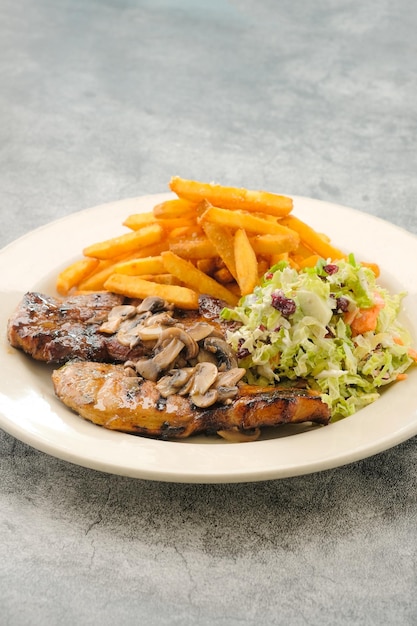 Spezialität gegrilltes Schweinekotelett mit Salat und Pommes frites, serviert in Gericht isoliert auf der Hintergrundseite