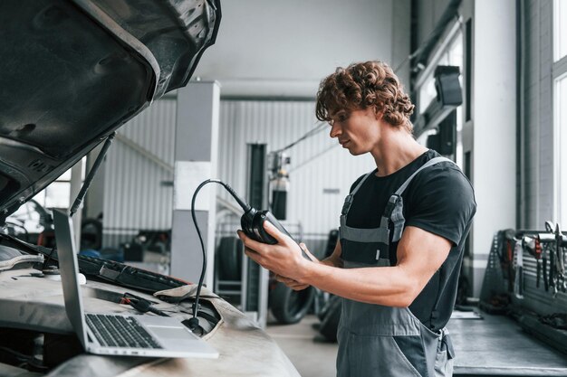 Spezialwerkzeug zum testen von merkmalen erwachsener mann in grauer uniform arbeitet im autosalon