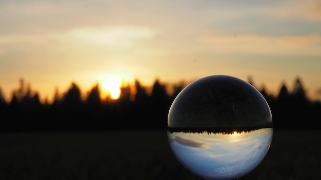 Sphärische Linse (Kristallkugel) und farbenfroher Sonnenuntergang vor dem Hintergrund des Waldes.