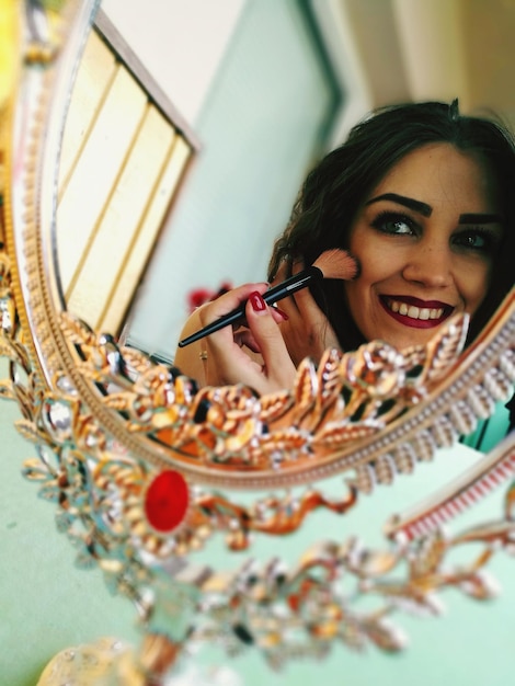 Spiegelbild einer lächelnden jungen Frau im Spiegel, die sich im Gesicht schminkt