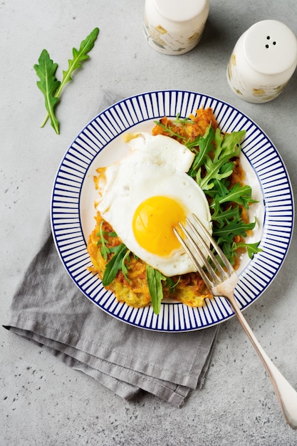 Spiegelei mit Kartoffelpuffer, Rucola und Avocado auf Keramikplatte zum Frühstück. Draufsicht.