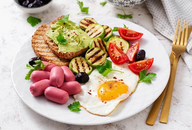 Spiegelei mit Miniwurst, Tomaten, gegrillten Zucchini, schwarzen Oliven und Toast mit Guacamole English Breakfast Brunch