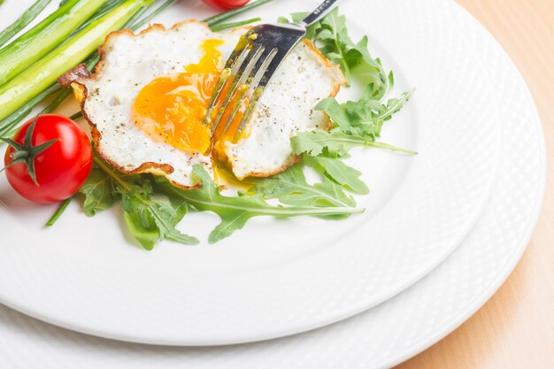 Spiegelei mit Tomaten und grünem Salat auf weißem Teller