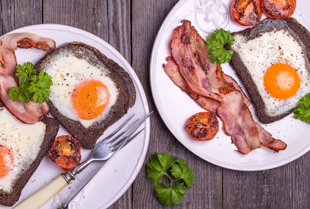 Spiegeleier in Roggenbrot mit Speck, Tomaten und Petersilie im rustikalen Stil.