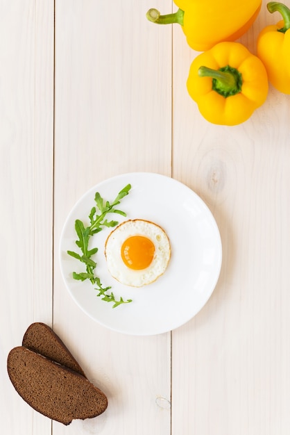 Spiegeleier mit Rucola-Paprika und Brot auf einem Holztisch