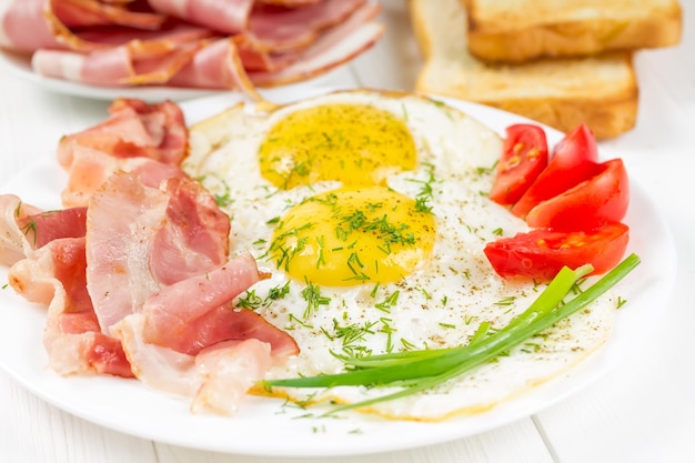 Spiegeleier mit Schinken und Tomaten auf einem weißen Teller