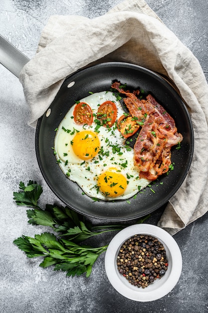 Spiegeleier mit Speck in einer Pfanne. Keto-Diät. Keto Frühstück. Low Carb Diät-Konzept. Vielfett-Diät. Grauer Hintergrund. Draufsicht