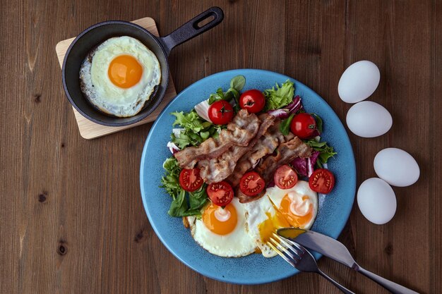 Spiegeleier mit Specksalat und Kirschtomaten auf blauem Teller