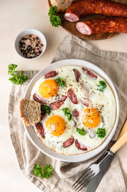 Spiegeleier mit Wurst und Petersilie auf einem Keramikteller serviert mit Brot Klassisches Frühstück