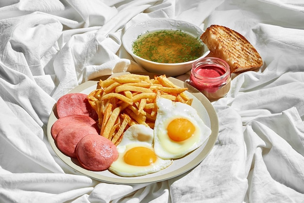 Spiegeleier mit Wurstpommes auf einem Teller auf einem weißen Blatt Hartes Licht