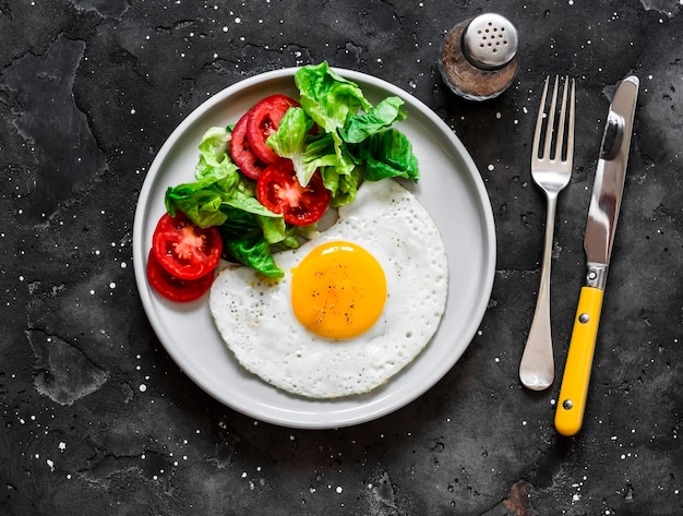 Spiegeleierspeck des Frühstückstellers und Gemüsesalat auf einer Draufsicht des dunklen Hintergrundes Beschneidungspfad eingeschlossen