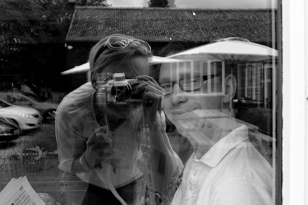 Spiegelung einer Frau, die vor einem Mann fotografiert, gesehen durch ein Glasfenster