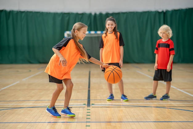 Spiel. ein mädchen, das mit einem ball spielt und beteiligt schaut, während freunde warten