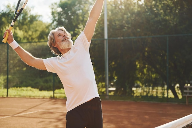 Spiel spielen Älterer, moderner, stilvoller Mann mit Schläger im Freien auf dem Tennisplatz tagsüber