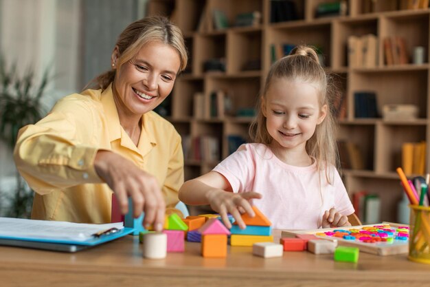 Spiel- und Bildungskonzept Positive Lehrerin trainiert mit intelligentem Mädchen, das hölzerne Entwicklungsblöcke spielt