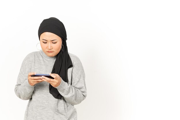 Spielen des Handyspiels auf dem Smartphone der schönen asiatischen Frau, die Hijab trägt, lokalisiert auf weißem Hintergrund