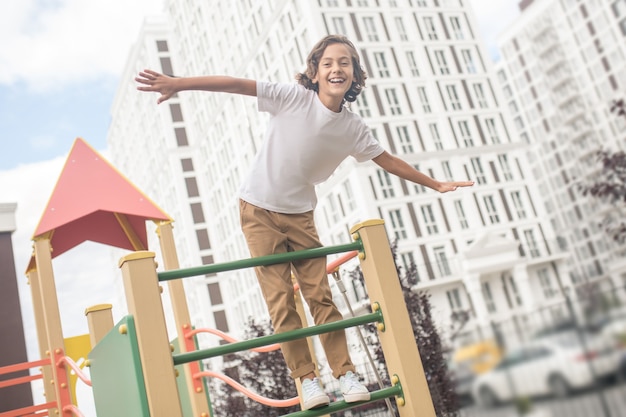 Spielen. Netter Junge in einem weißen T-Shirt auf einem Spielplatz