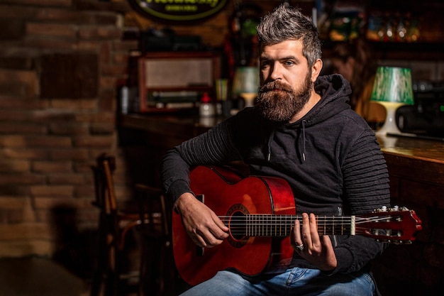 Spielen Sie den Gitarrensänger singen Beard Hipster Mann sitzt in einer Kneipe Live-Musik Gitarren und