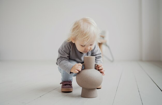 Spielen zu Hause mit einer Blumenvase. helles und stilvolles Interieur der Wohnung. kleine Tochter ist ein blondes kaukasisches Mädchen in einem stilvollen beigen Kleid